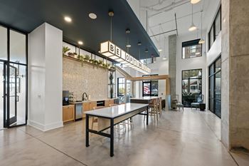 A modern interior space with a long table and chairs, a counter, and a plant hanging from the ceiling.